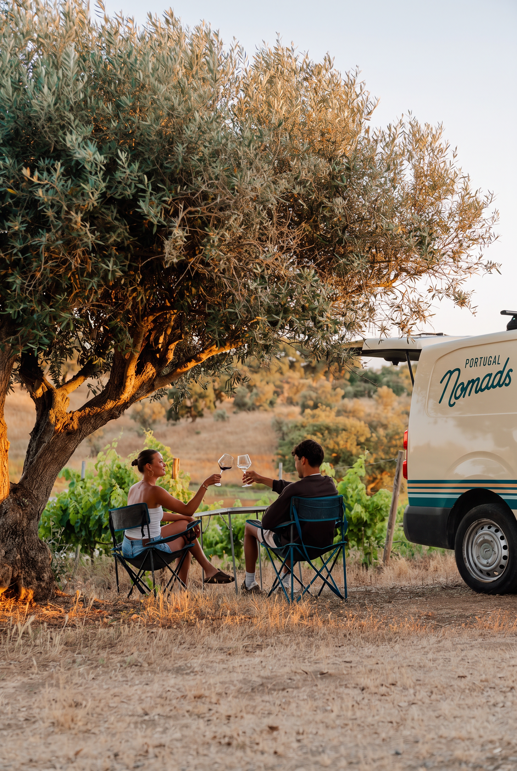 couple toasting wine by a campervan in a vineyard at sunset